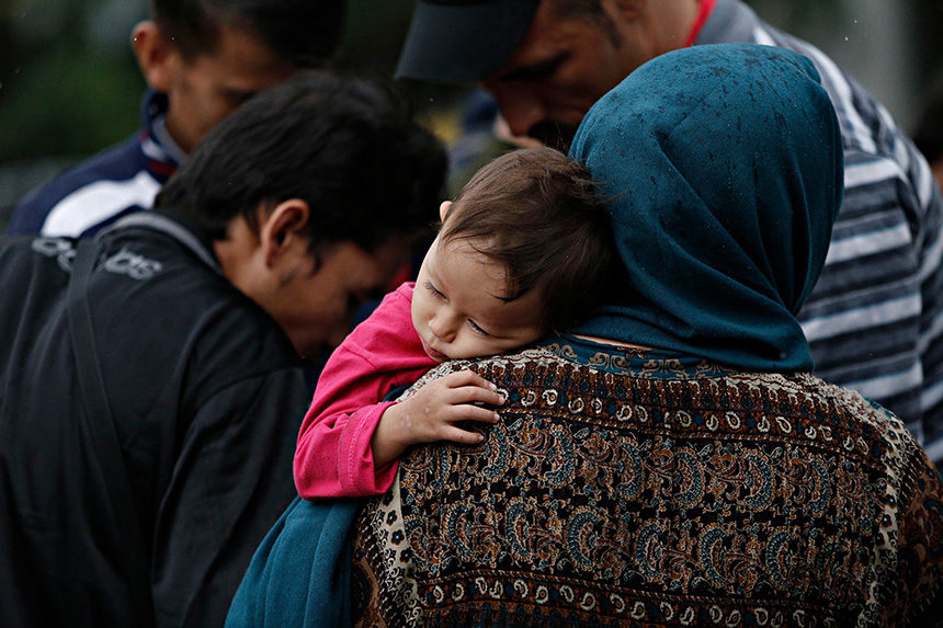 A small Afghan child holds onto their mother as they wait with other refugees.