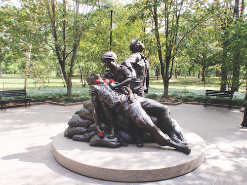 Roses lay atop a statue of Vietnam War nurses as they tend to a wounded soldier.