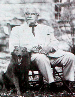 Colonel Sanders with a dog and in a rocking chair.