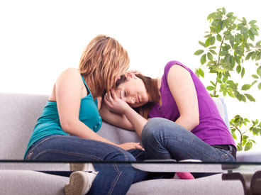 woman comforting teenage daughter while they sit on a couch