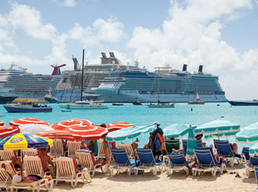 people under umbrellas on sand looking out at cruise ship on the ocean