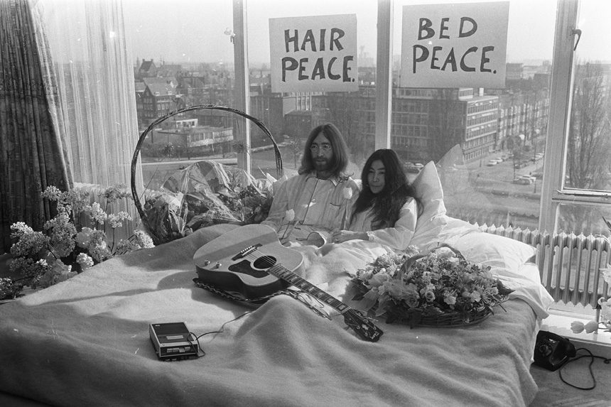 John Lennon and Yoko Onno in a bed with a guitar and flowers.