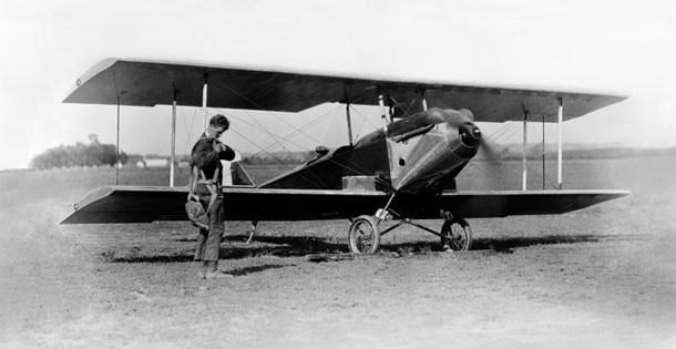 Charles Lindbergh adjusts his parachute in front of Sergeant Bell’s experimental biplane on Lambert Field, St. Louis, Missouri, in the mid-to-late 1920s, while Bell waits in the plane.