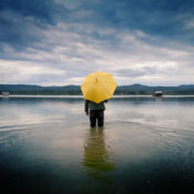 Person standing alone in a lake with his back to the camera and holding a yellow umbrella