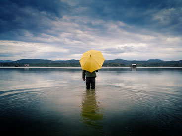 Person standing alone in a lake with his back to the camera and holding a yellow umbrella
