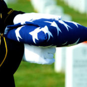 A military officer in white gloves holds a folded American flag at a military funeral.