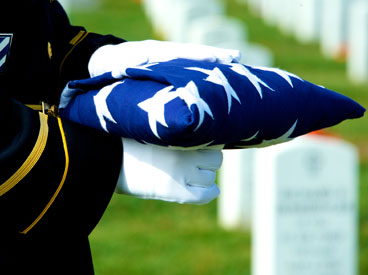 A military officer in white gloves holds a folded American flag at a military funeral.