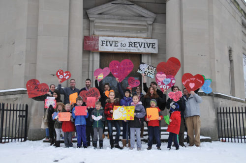 YPA members stand in front of a library with a sign that says "Five to Revive"
