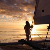 A girl on a sailboat is looking at the setting sun.