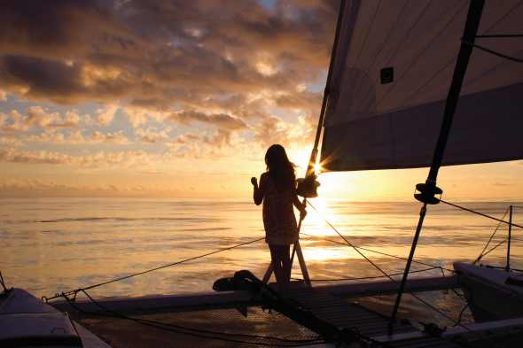 A girl on a sailboat is looking at the setting sun.