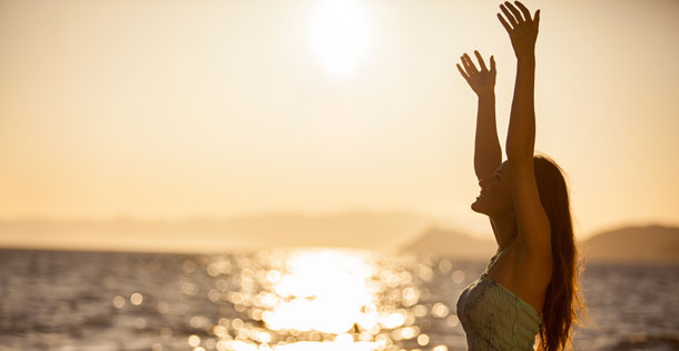 Young, happy woman on a beach at sunset, raising her hands in the air