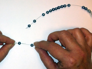 hands holding beads, crimp bead, and magnetic clasp on wire