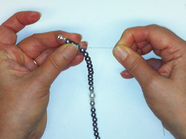hands holding beads, crimp bead, and magnetic clasp on wire