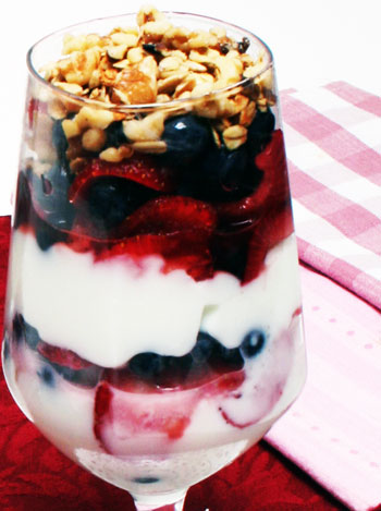 strawberries, blueberries, yogurt, granola in parfait glass