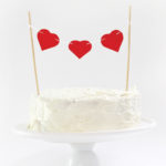 three paper hearts strung together on top of cake