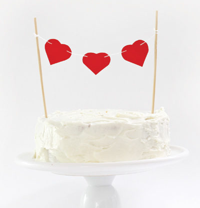 three paper hearts strung together on top of cake
