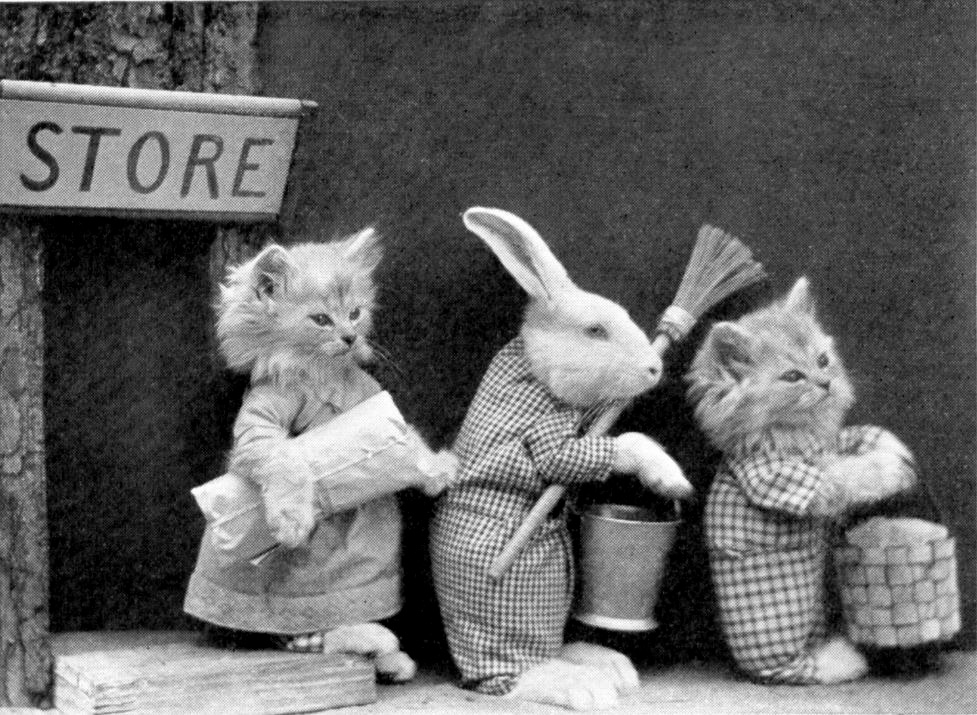 Two kittens and a bunny walk out of a store with a broom, a couple of buckets, and a sack.