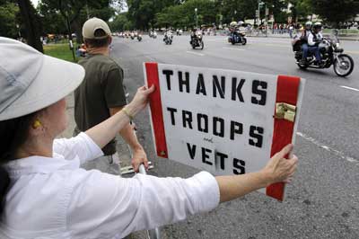 A woman at a parade holding a side thanking veterans.