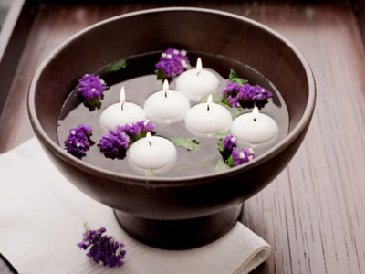 A bowl of lit candles and lilacs.