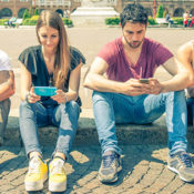 Teenagers sitting outdoors and texting with their smartphones