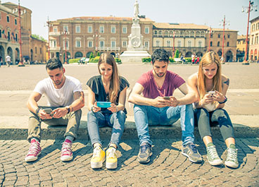 Teenagers sitting outdoors and texting with their smartphones