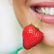Young woman holding a strawberry between her teeth by its stem. Source: Shutterstock.com