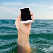 The hand of a submerged swimmer sticks their iPhone out of the water.
